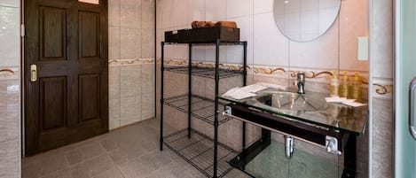 A bathroom with a wooden door, a glass sink, a mirror, and a metal shelf unit.