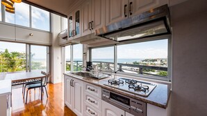 A modern kitchen with white cabinets, a stainless steel range hood, and a large window overlooking a scenic view. - E-horizon Resort Condominium Yomitan (Yomitan)