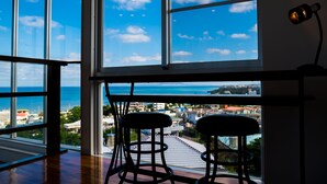 A room with large windows overlooking a coastal cityscape, two bar stools, and a table. - E-horizon Resort Condominium Yomitan (Yomitan)