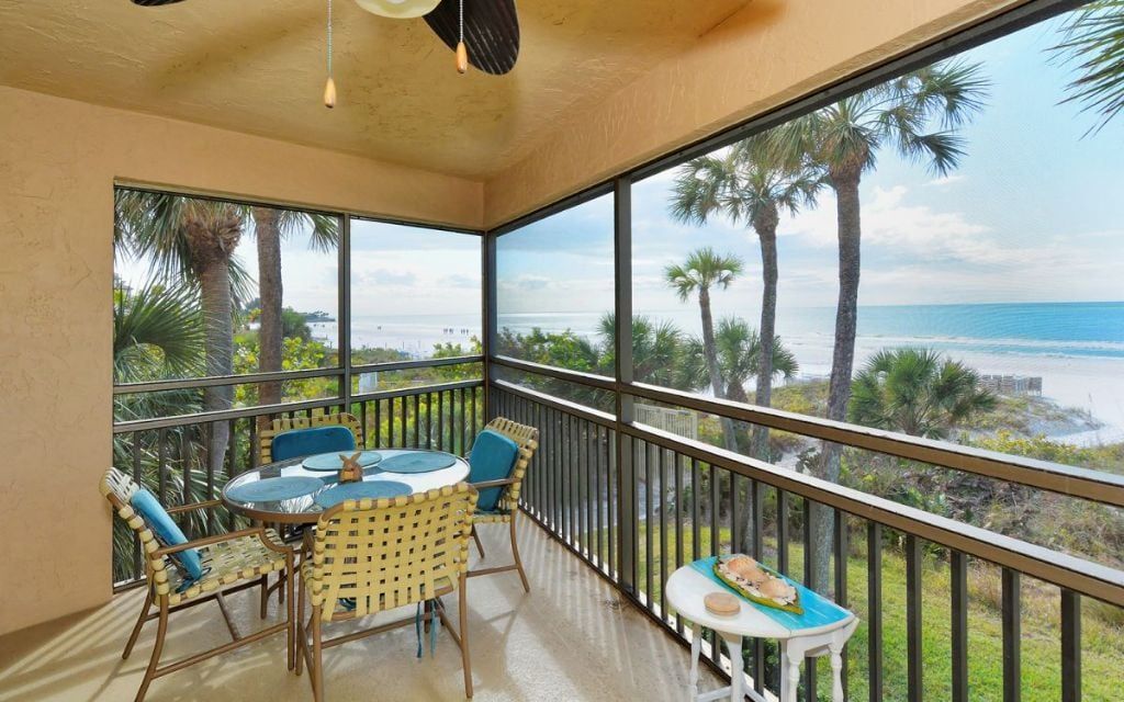 Een balkon met een tafel en stoelen, met uitzicht op een strand met palmbomen en de oceaan.