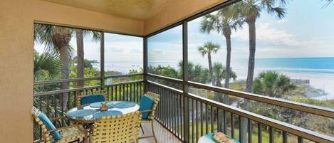 Een balkon met een tafel en stoelen, met uitzicht op een strand met palmbomen en de oceaan.