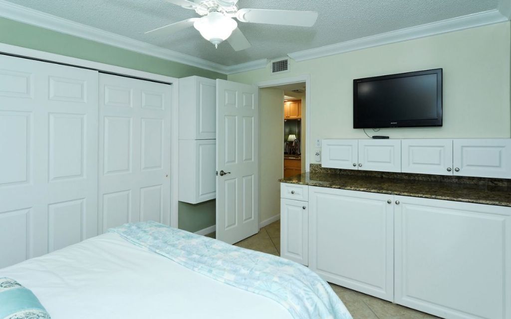 Une chambre à coucher avec un lit, un ventilateur de plafond et un téléviseur fixé au mur.
