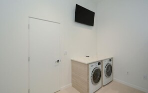 Une buanderie équipée de deux machines à laver, avec une porte blanche et un téléviseur fixé au mur.