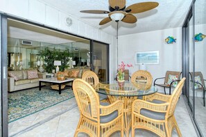 A modern living room with a glass dining table surrounded by wicker chairs, a sofa, and a coffee table.