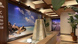 A reception area with a large digital screen displaying a beach scene, a reception desk, and a potted plant. - Hotel Palms - Adults Only (Moriyama)
