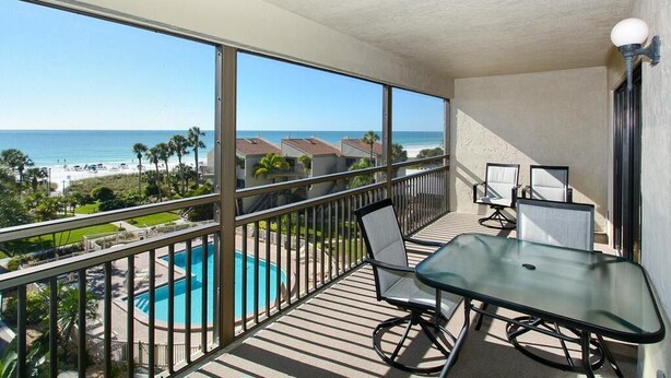 Ein Balkon mit Glastisch und Stühlen, mit Blick auf ein Schwimmbad und einen Strand.