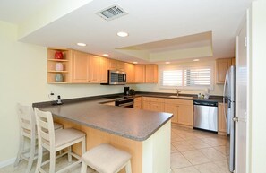 A modern kitchen with a central island, wooden cabinets, stainless steel appliances, and a window with blinds.