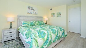 Ein Schlafzimmer mit einem Bett, zwei Nachttischen und einem Beistelltisch. Darüber am Bett befinden sich Wandbilder und rechts ist eine Tür.