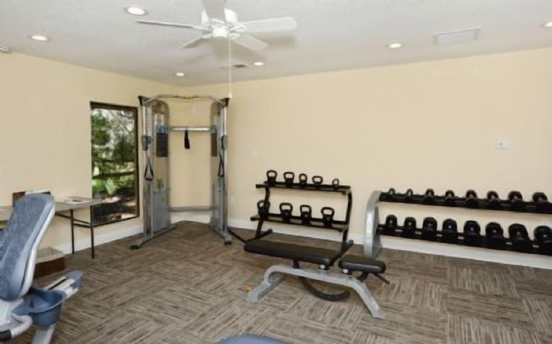 A gym with exercise equipment, a ceiling fan, and a wall-mounted dumbbell rack.