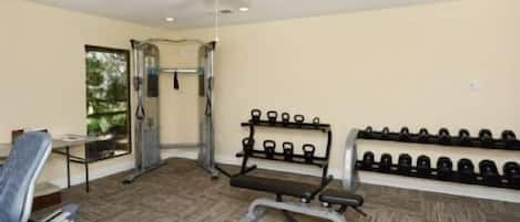 A gym with exercise equipment, a ceiling fan, and a wall-mounted dumbbell rack.