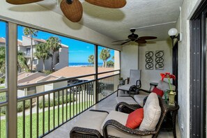 A balcony with wicker furniture, a ceiling fan, and a view of the ocean.