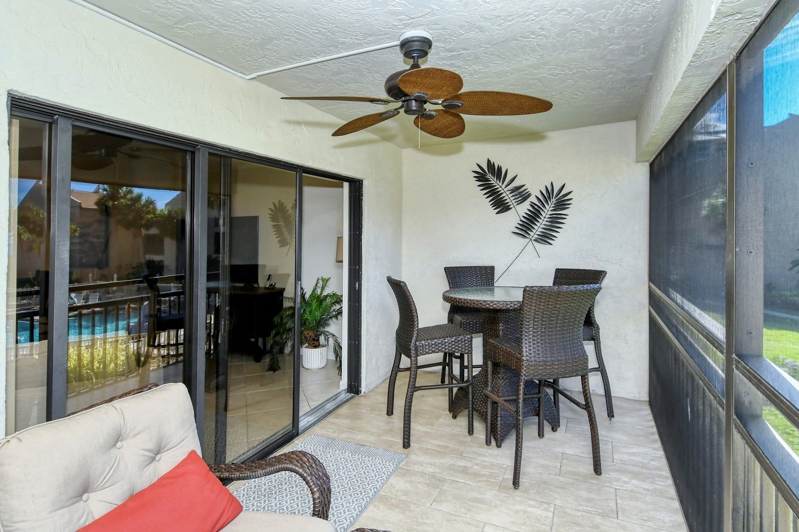 A room with a ceiling fan, a dining table with chairs, a sofa, and a sliding glass door leading to a pool area.
