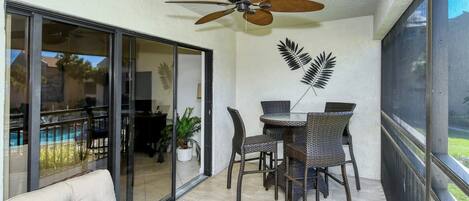 A room with a ceiling fan, a dining table with chairs, a sofa, and a sliding glass door leading to a pool area.