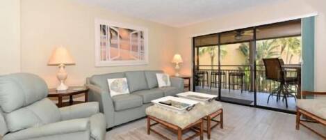 A living room with a sofa, armchair, coffee table, and a dining area with chairs and a table.