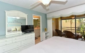 Une chambre à coucher avec un lit, une télévision, une commode et un balcon équipé de chaises.