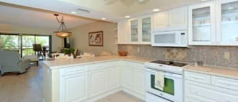 A kitchen with white cabinetry, a large island, a ceiling fan, and a view to the dining area.