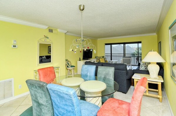 A living room with a glass table, colorful chairs, a sofa, and a television.