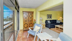 Ein Balkon mit Blick auf Gebäude, ein Holzschrank, ein blauer Stuhl, ein schwarzes Sofa und ein weißer Tisch.