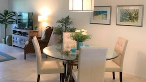 Un coin repas avec une table ronde, quatre chaises, un luminaire suspendu et un téléviseur en arrière-plan.