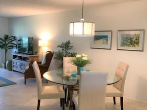 Un coin repas avec une table ronde, quatre chaises, un luminaire suspendu et un téléviseur en arrière-plan.