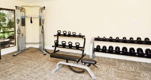 Une salle de sport équipée d’un support à squats, d’un banc de développé couché et d’haltères.