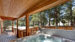 Una terraza de madera con un jacuzzi y vistas a un área boscosa.