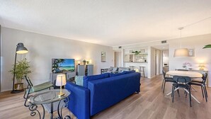 Een moderne woonkamer met een blauwe bank, een glazen salontafel, en een eethoek met een tafel en stoelen.