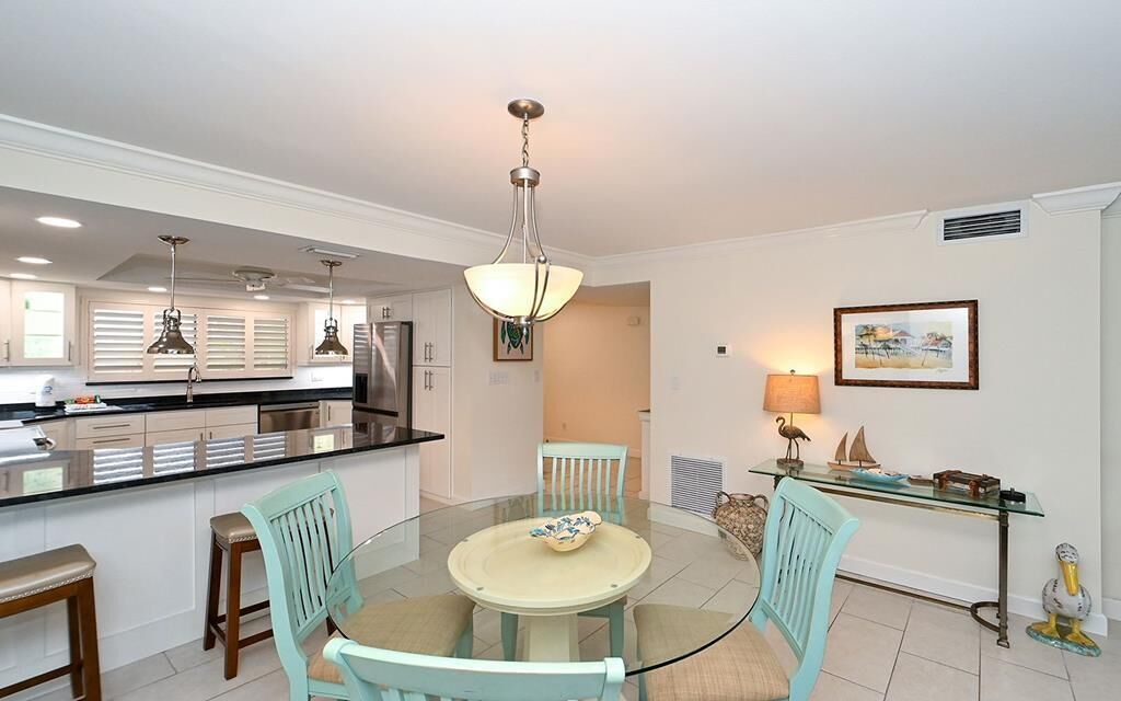 A modern kitchen with a central island, pendant lighting, and a dining area with a glass table and chairs.