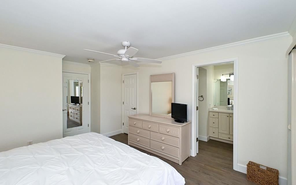 A bedroom with a bed, dresser, mirror, ceiling fan, and a door leading to a bathroom.