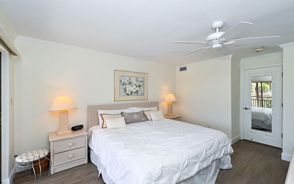 A bedroom with a bed, two bedside tables with lamps, a ceiling fan, and a door leading to a balcony.