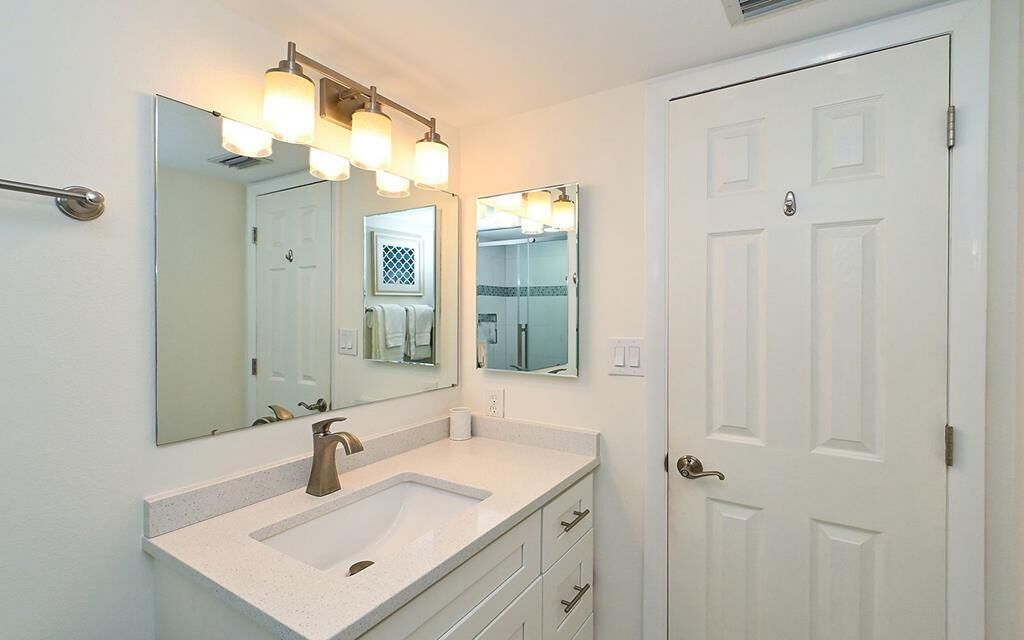 A bathroom with a white sink, two mirrors, and a white door.