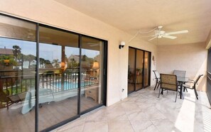 A balcony with a glass door, a ceiling fan, and a dining area with chairs and a table.