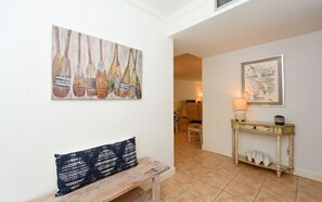 A hallway with a bench, a console table with a lamp, and two artworks on the walls.
