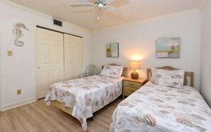 Ein Schlafzimmer mit zwei Einzelbetten, einem Deckenventilator, einem Nachttisch und einer Wandlampe.