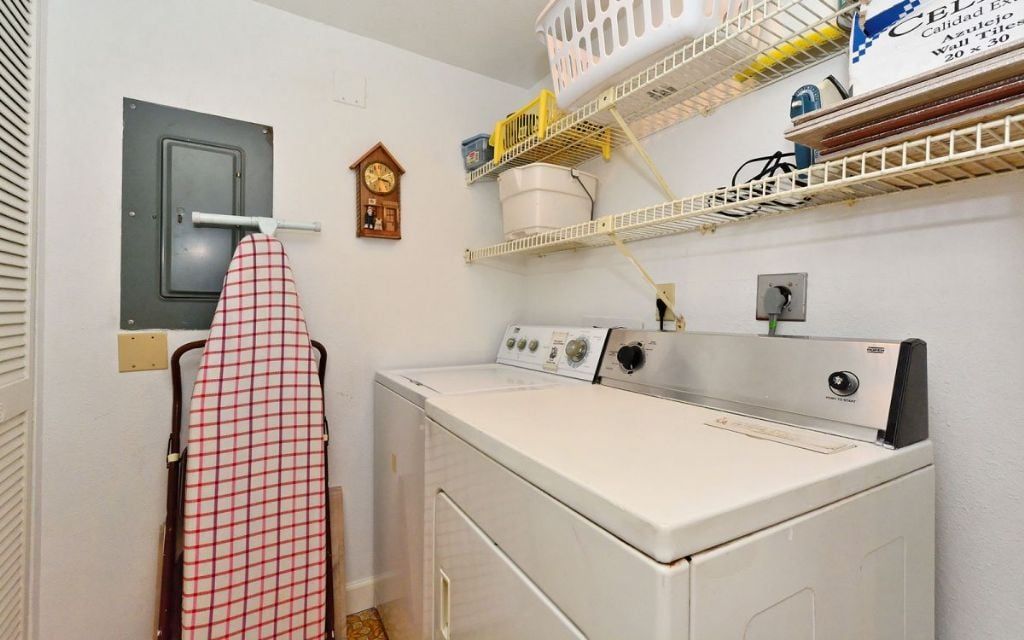 Un cuarto de lavado con lavadora, tendedero y estantes con diversos artículos.