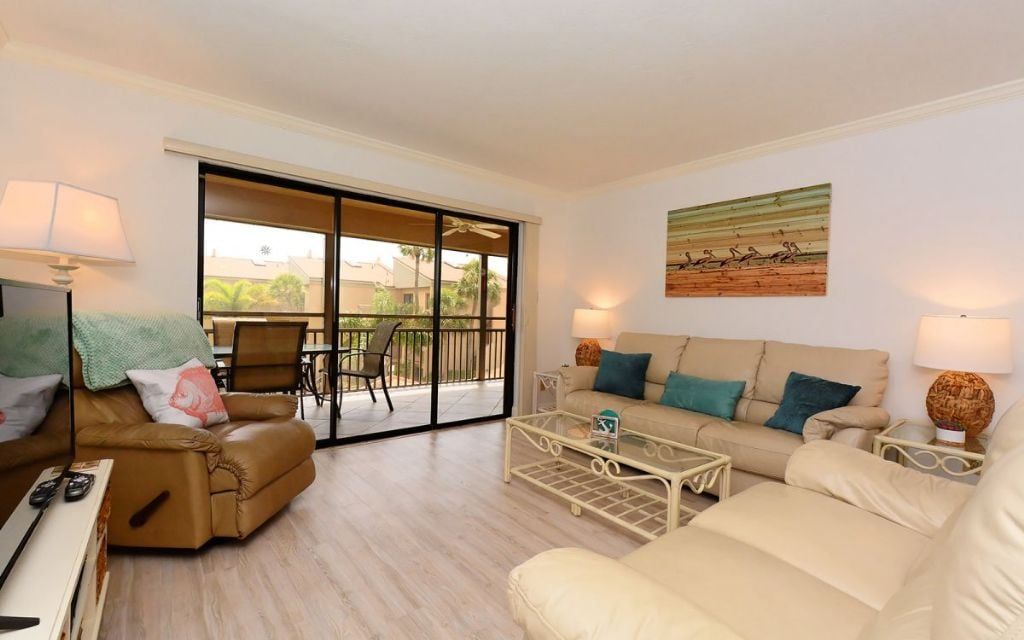 A living room with a sofa, armchair, coffee table, and a sliding glass door leading to an outdoor area.