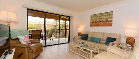 A living room with a sofa, armchair, coffee table, and a sliding glass door leading to an outdoor area.