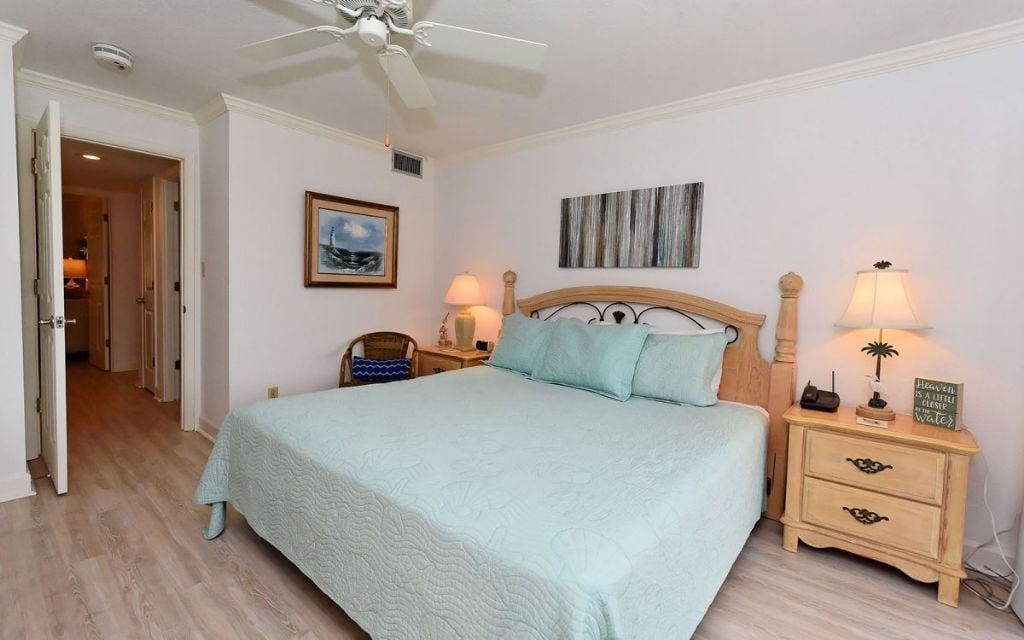 Ein Schlafzimmer mit einem Bett, Nachttischen, einem Deckenventilator und einer Tür zu einem anderen Raum.
