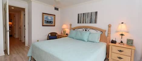 A bedroom with a bed, bedside tables, a ceiling fan, and a door leading to another room.