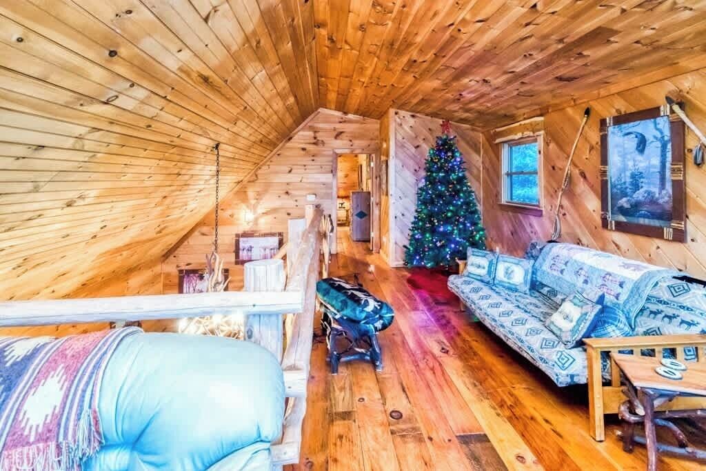 L’intérieur d’un chalet accueillant, avec un plafond en bois, un canapé, une petite table, un sapin de Noël et une fenêtre.