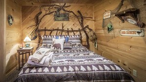Camera di una baita in legno con un letto, un comodino e decorazioni a parete tra cui un orso e un cartello con un cervo che attraversa la strada.