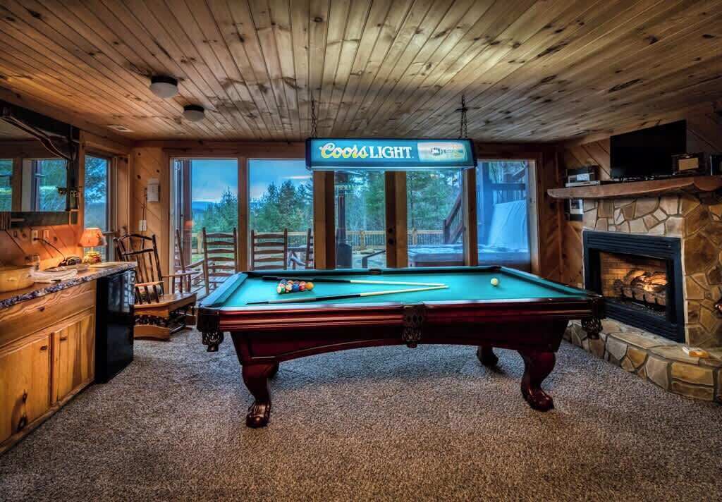 Une table de billard ornée d’une enseigne Coors Light, une cheminée et une vue sur l’extérieur.