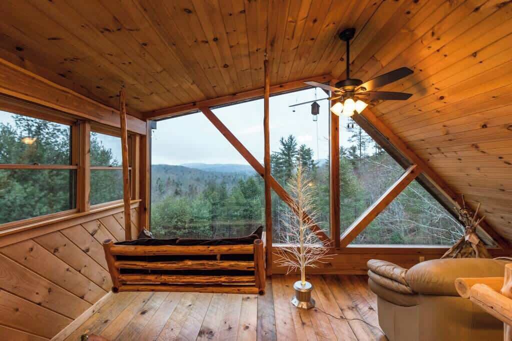 Eine Holzhütte mit geneigtem Dach, großen Fenstern, einem Deckenventilator und einer Sitzbank.