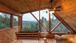 Una baita in legno con tetto spiovente, ampie finestre, una ventola a soffitto e una panca.