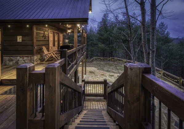 A wooden cabin with a porch, a staircase, and a view of a forested area.