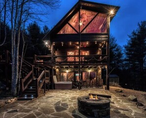A multi-level wooden cabin with a stone fire pit and outdoor seating area.