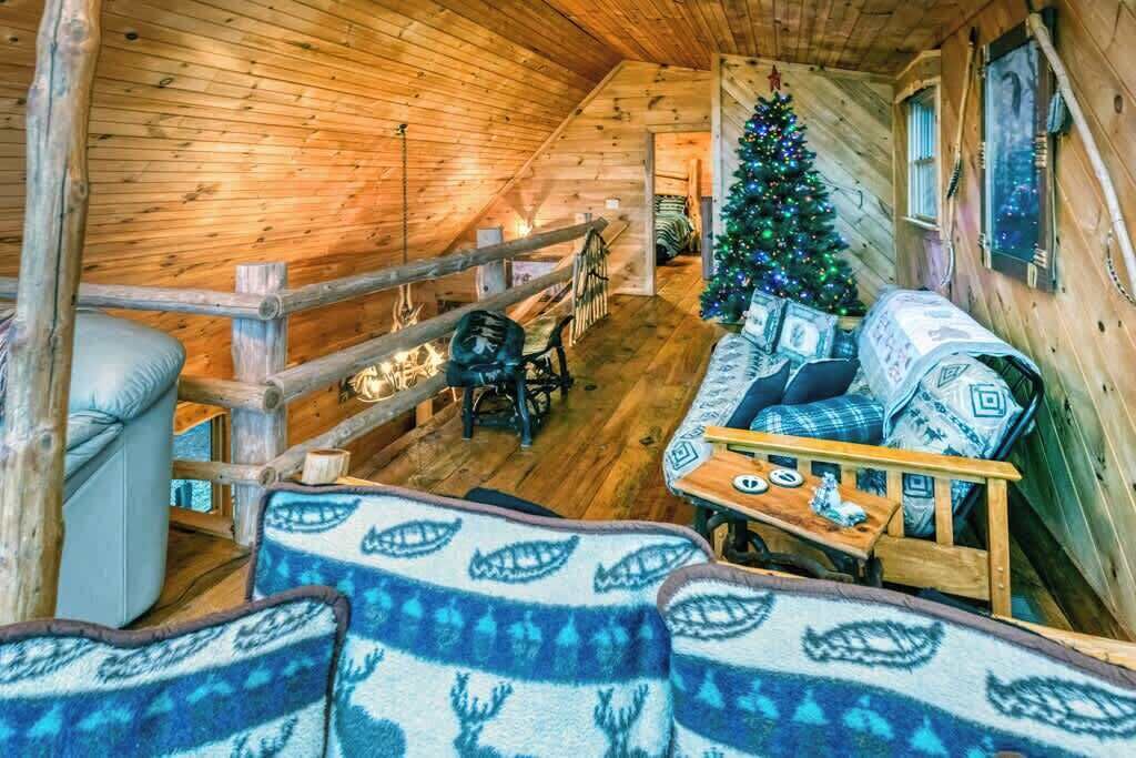 A cozy cabin interior with a wooden interior, a Christmas tree, a sofa, and a dining table.
