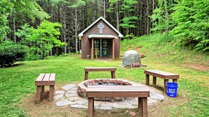 Eine rustikale Holzhütte mit Feuerstelle, Picknicktischen und einem Kruzifix an der Tür.