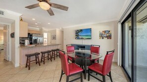 Uma área de refeições com mesa redonda e cadeiras vermelhas, cozinha ao fundo e uma janela grande com vista.