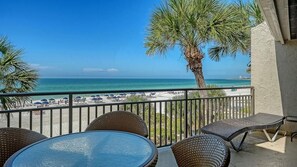 Ein Balkon mit Korbmöbeln, der auf einen Strand mit Sonnenschirmen und Palmen blickt.